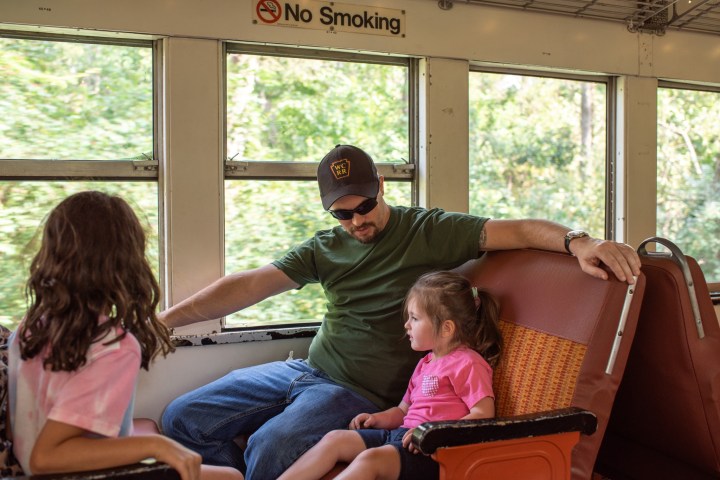 Man and two children on a train, seated by windows with a 'No Smoking' sign above.