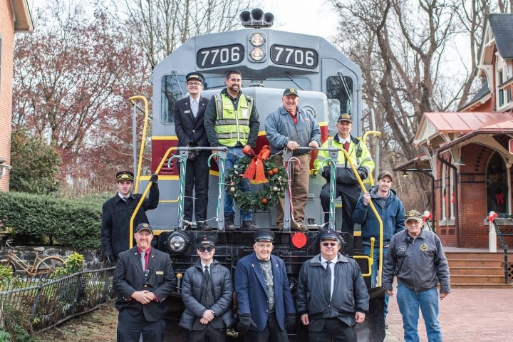 Group of people posing in front of train at a historic train station.