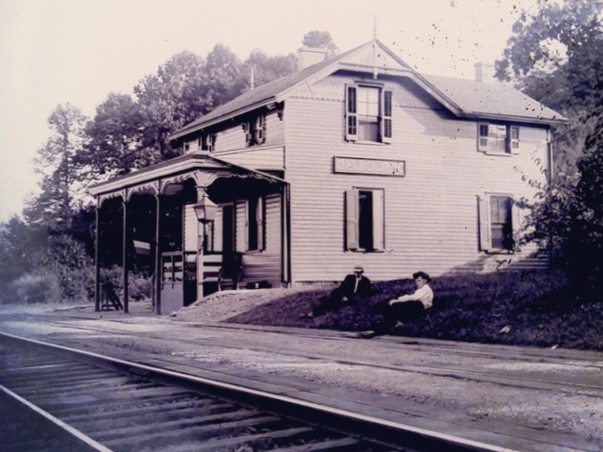 Vintage train station with two people sitting outside near tracks.