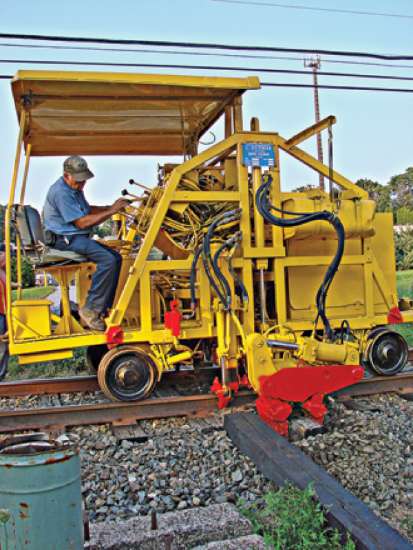 Person operating yellow railway maintenance machine on tracks.